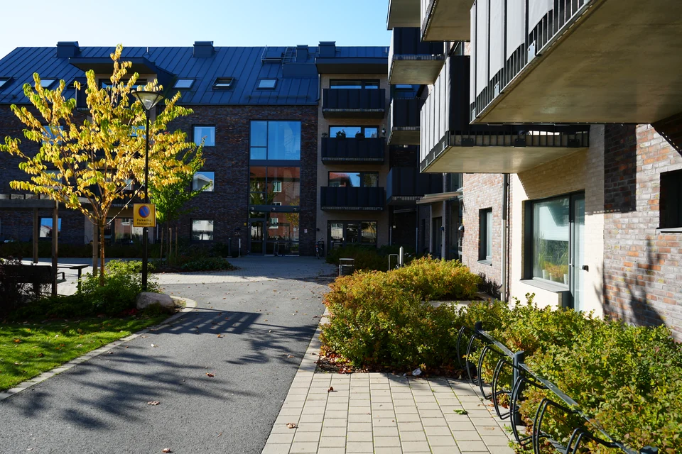 Robins kamerafotografi av samma innergård på Uttern, med glasentrén, balkongerna och trädet i höstfärg.